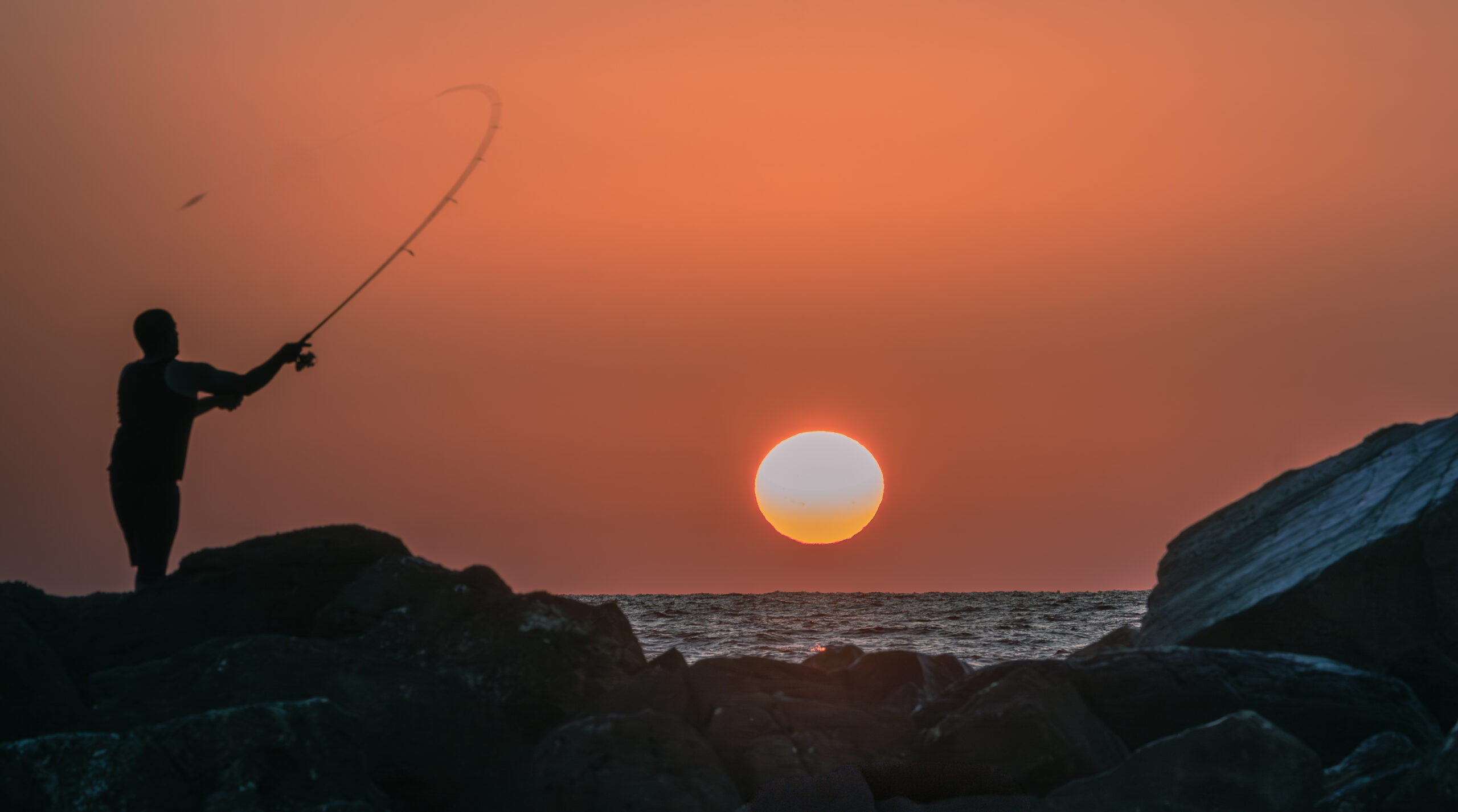 Silhouette of a fisherman casting a line at sunset over the Mediterranean in Tel Aviv, Israel.