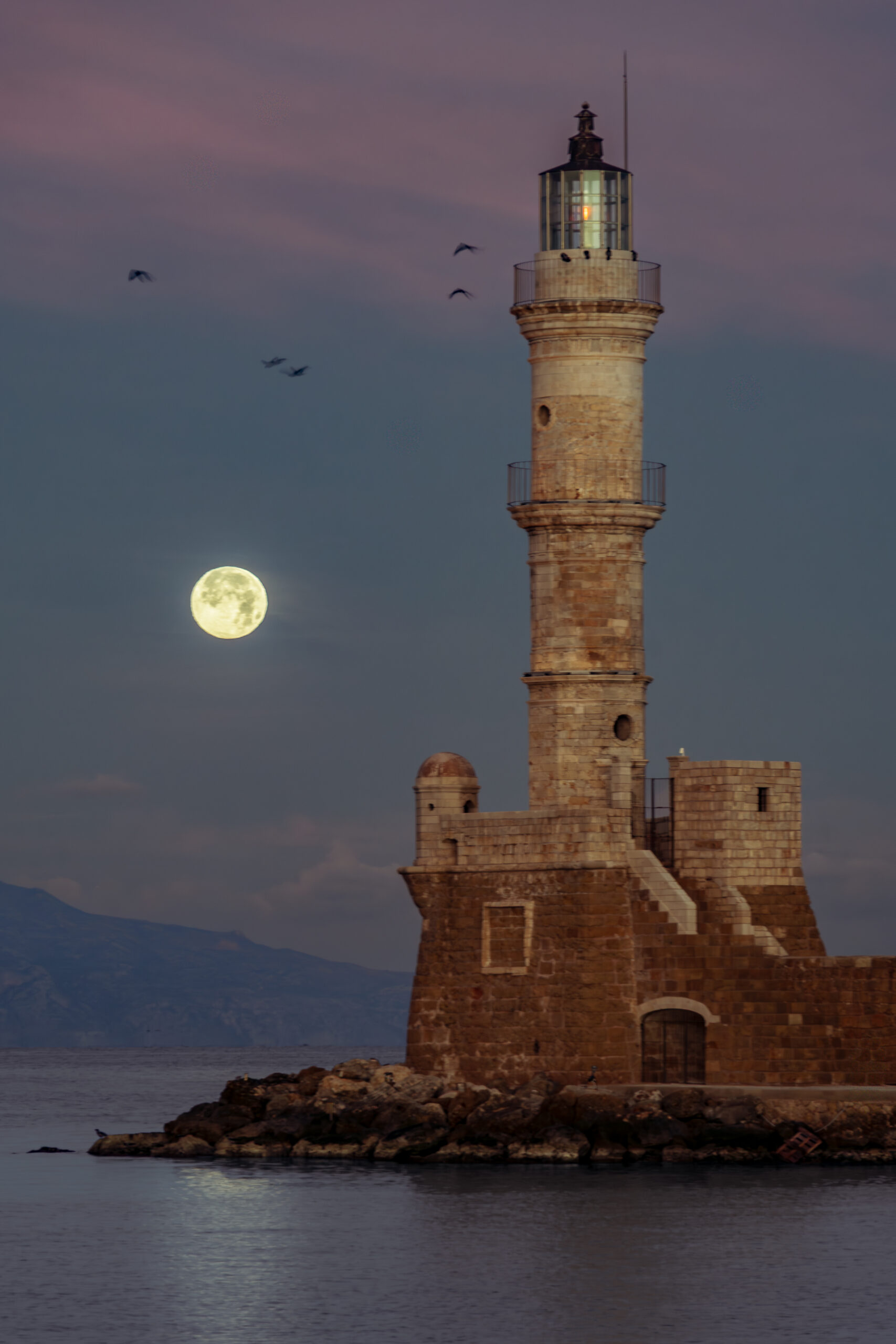 Lighthouse at night in Chania Harbor, Crete, Greece, illuminated by moonlight.