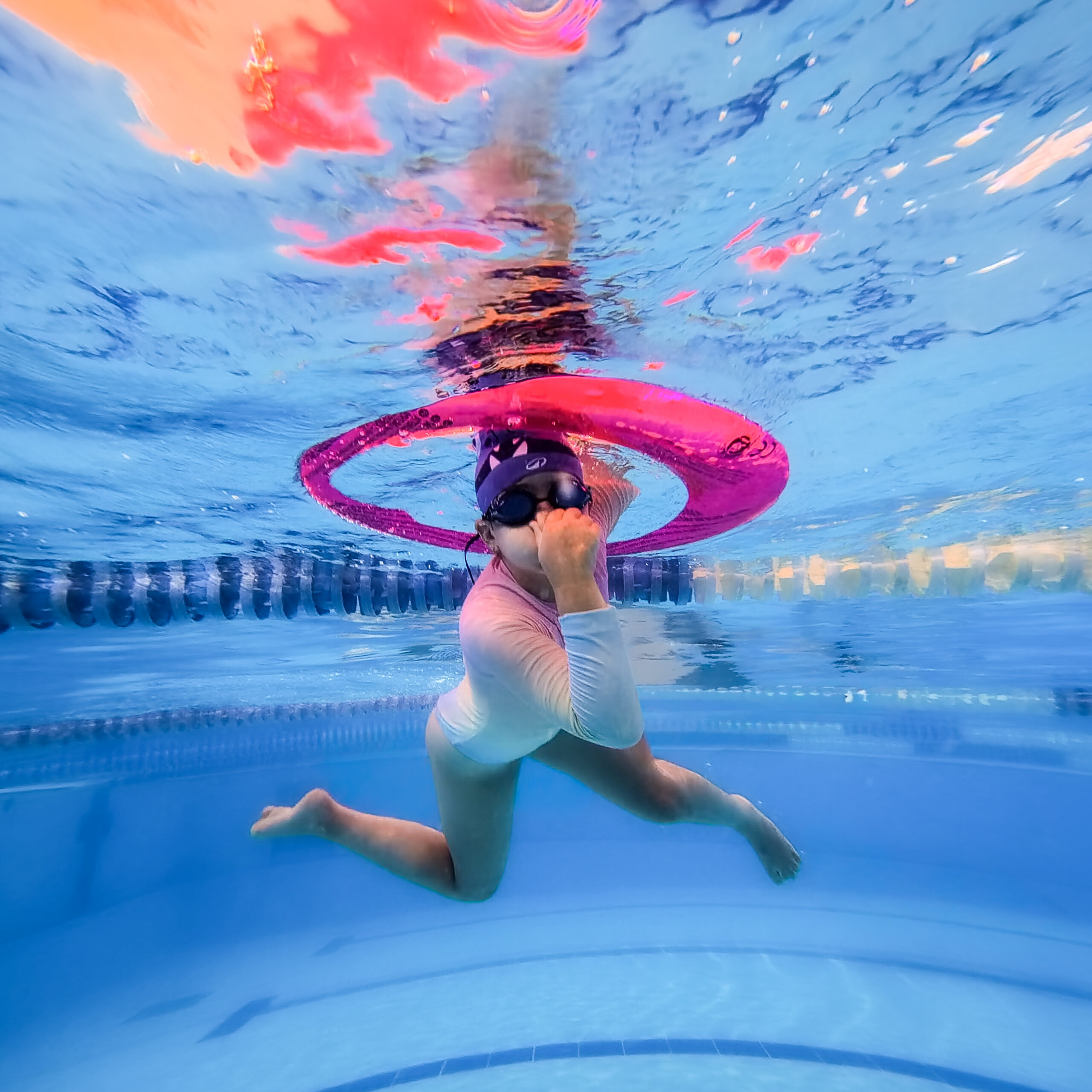 Young girl underwater in a swimming pool surrounded by colorful reflections.