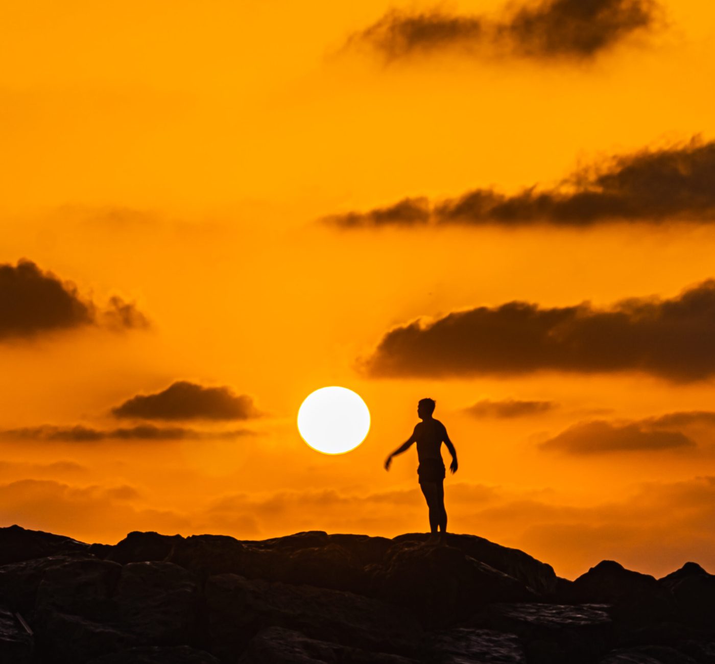 Silhouette of a person standing on a breakwater at sunset in Netanya, Israel.