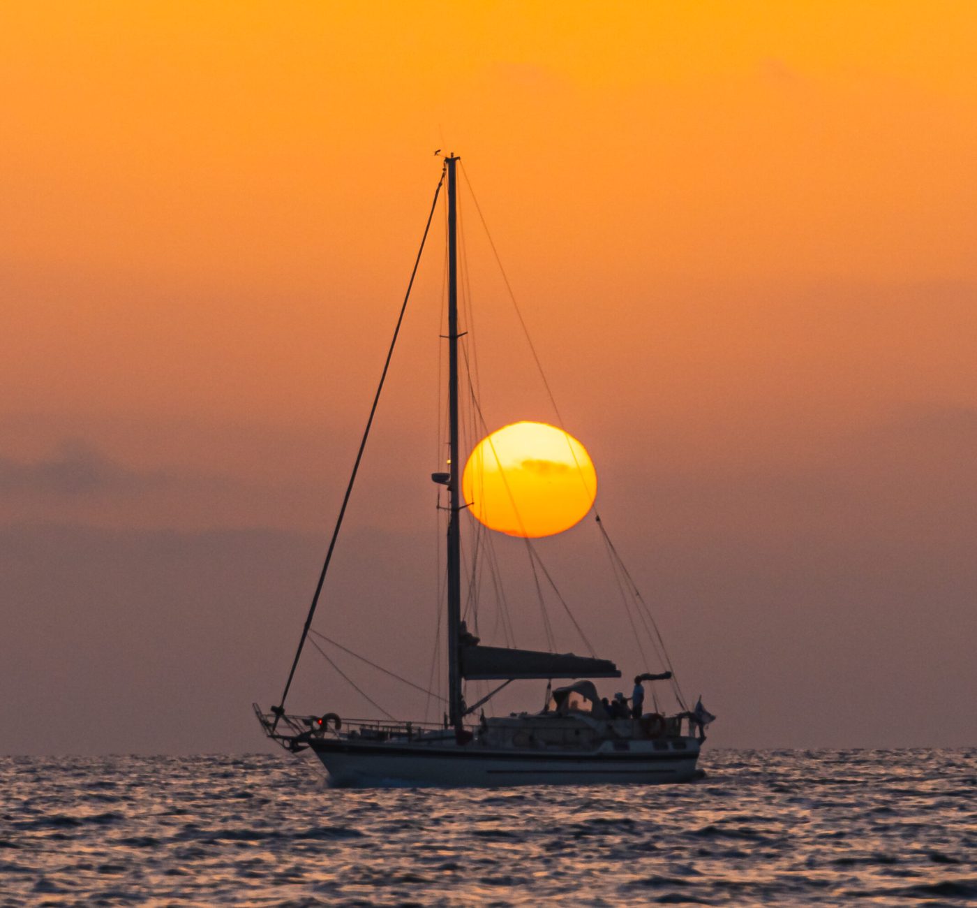 Sailboat aligned with the setting sun over the Mediterranean Sea in Netanya, Israel.