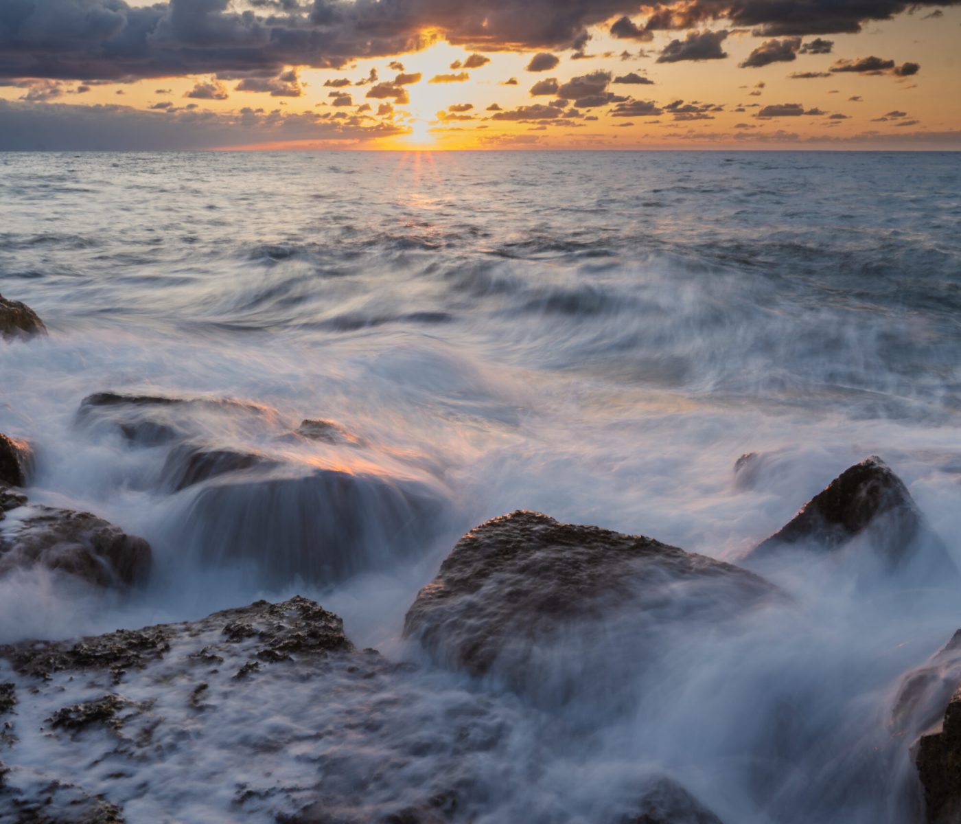 Long-exposure sunset over the rocky Mediterranean coast in Tel Aviv, Israel.