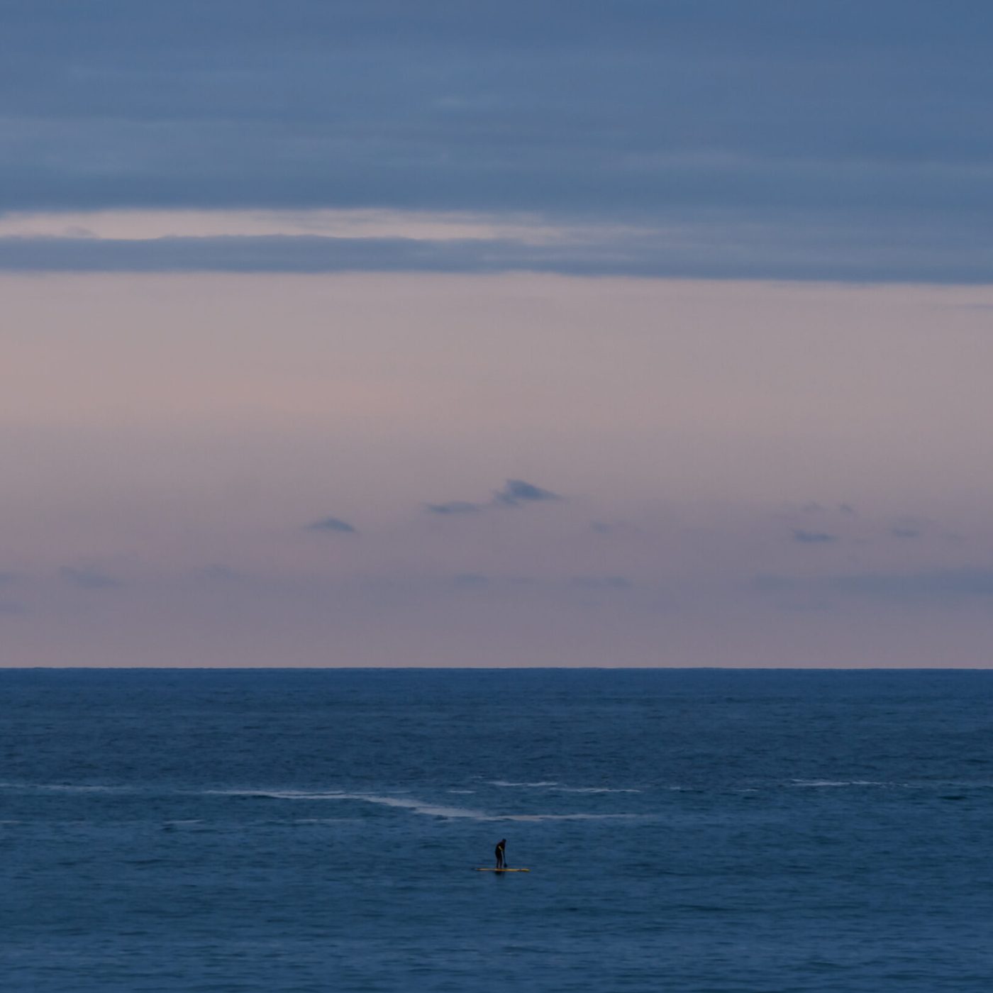 Lone paddleboarder crossing the calm waters of La Concha Bay in San Sebastián, Spain.
